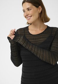 Haut noir à manches longues avec des rayures horizontales texturées, présentant des motifs complexes et un col arrondi. Sections légèrement transparentes.