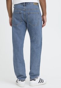 Vaaleansiniset farkut, joissa on rento istuvuus, viisi taskua ja ompeludetaljit. Yhdistetty valkoisiin kenkiin. Takakuvassa.