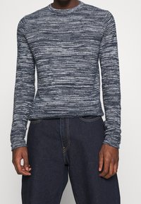 Granatowy, długi sweter z teksturowanym, melanżowym wzorem. Okrągły dekolt i dopasowane mankiety, zestawiony z ciemnymi dżinsami.