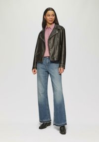 Zwarte leren motorjack met zilveren rits, roze overhemd met kraag, lichtblauwe flare jeans en zwarte enkellaarsjes. Eenvoudige en casual outfit.
