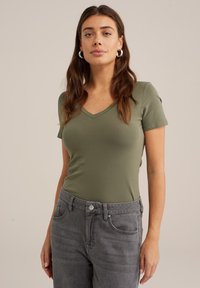 T-shirt vert olive à col en V en coton doux, style ajusté, manches courtes, associé à un jean en denim gris taille haute avec poches avant.