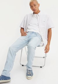 Korte mouwen, gestreept overhemd in wit, roze en blauw, gedragen over een wit T-shirt met lichtblauwe jeans en blauwe sneakers.