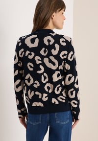 Pull à imprimé léopard en marine et crème, en tissu tricot doux, avec un ourlet et des poignets côtelés, offrant une coupe décontractée.