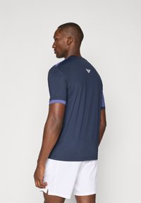 T-shirt atlético azul-marinho com mangas curtas, apresentando um detalhe roxo nas mangas e um logotipo na parte de trás. Feito de um tecido leve e suave.