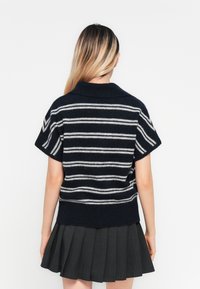 Pull rayé bleu marine et gris à manches courtes et col, fabriqué en tissu tricot doux, associé à une jupe plissée grise.
