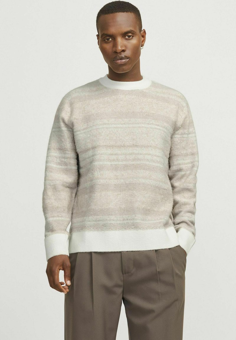 Pull en beige clair avec un motif rayé horizontal dans une texture douce. Il présente un col rond et des poignets et un ourlet côtelés blancs.