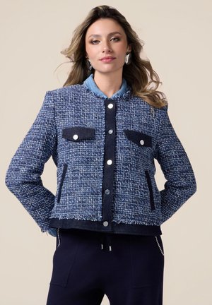Veste bleu texturée avec un col en denim contrastant, deux poches avant, boutons en argent et détail d'ourlet effiloché.