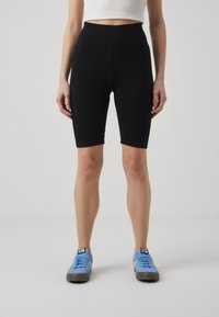 Black high-waisted bike shorts made of stretchy fabric, featuring a smooth texture and a form-fitting design, paired with blue sneakers.