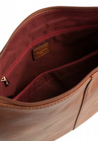 Bruine leren tas interieur met een kastanjebruine stofvoering, voorzien van een ritszak en een klein label. Soepele textuur, gestructureerd ontwerp.