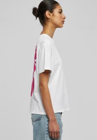 Hvit bomulls T-skjorte med korte ermer og rund hals, med et stort rosa grafisk design på baksiden.
