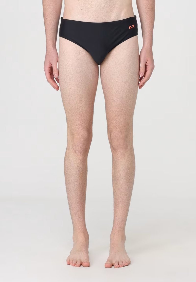 Slip da bagno neri con un design a vita bassa, caratterizzati da un logo arancione sul fronte. Il tessuto sembra liscio e aderente.