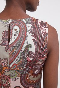 Vêtement sans manches avec un imprimé cachemire multicolore en rouge, vert et beige. Dispose d'un détail en forme de serrure au dos et d'une texture de tissu lisse.