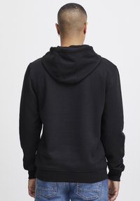 Sudadera con capucha negra de tejido suave, con un bolsillo tipo canguro y puños acanalados. La parte posterior presenta un diseño liso sin adornos.