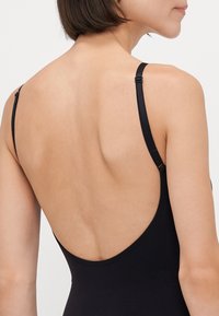 Black swimsuit with a low-back design, thin adjustable straps, and smooth fabric texture, highlighting a minimalist silhouette.