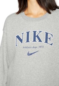 Grå sweatshirt i mjukt tyg, med "NIKE" i fet marinblå text och mindre text "Athletic dept. 1972" tillsammans med Nike swoosh-logotypen.