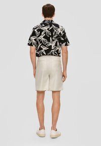 Czarna koszulka z krótkim rękawem w biały wzór liści, zestawiona z beżowymi szortami. Model odwrócony tyłem, w białych sneakersach. Prosty, casualowy wygląd.
