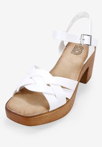 Sandali bianchi con tacco a blocco in legno marrone e cinturini intrecciati in materiale sintetico. Cinturino alla caviglia regolabile con fibbia argentata.