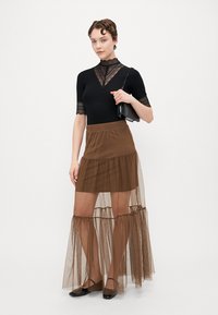 Svart blonde topp med korte ermer og høy hals, parret med en brun lagdelt tylskjørt, som har et gjennomsiktig overlag og ankel-lengde design.