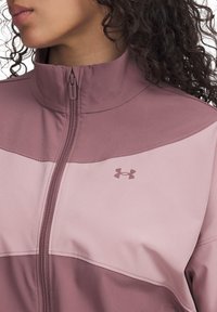 Light pink sports jacket with a high collar, half-zip closure, and contrasting dark pink upper panel. Features a small logo on the chest.