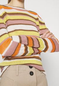Pull rayé dans des tons orange, jaune, rose et marron. Tricot léger avec un col rond et des manches longues, tissu textur�é.