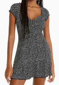 Svart klänning med vitt blommönster, korta ärmar, figursydd bodice, V-ringning och utsvängd kjol. Tillverkad av lättviktig tyg.