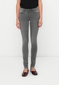 Grijze skinny jeans met een hoge taille, vijf zakken en een gladde, rekbare stof. Gecombineerd met glanzende bordeauxrode ballerina's.