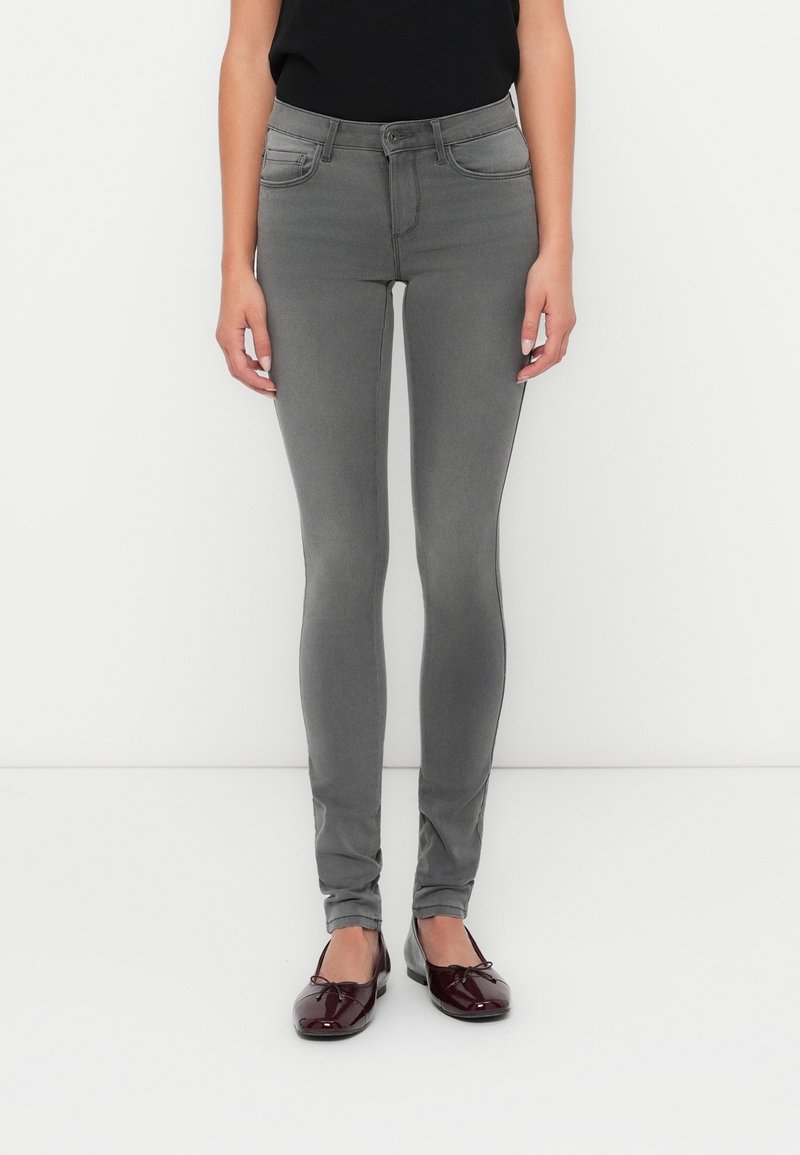 Grijze skinny jeans met een hoge taille, vijf zakken en een gladde, rekbare stof. Gecombineerd met glanzende bordeauxrode ballerina's.