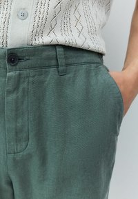 Pantaloni verzi din in, ușori, cu o textură netedă, având un buzunar în față și o închidere cu button la talie.