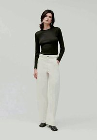 Melnas garās piedurknes blūze apvienota ar baltām platām biksēm. Apģērbs ir ar klasisku dizainu un gludu auduma tekstūru. Melna apavi noslēdz izskatu.