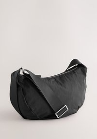 Black crescent-shaped crossbody bag with wide adjustable strap and zipper closure on a neutral background.
