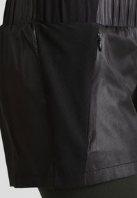 Svarta shorts i slät, glänsande material med en strukturerad, perforerad sidopanel. Har en dragkedjeficka för säker förvaring.