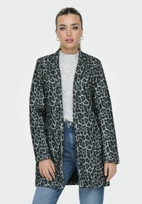Manteau à imprimé léopard avec une silhouette longue, une texture douce et un design ouvert, superposé sur un pull gris clair et un jean en denim.