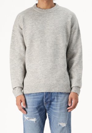 Pull en maille gris clair avec un col rond et un ourlet côtelé. Porté avec un jean bleu déchiré, doté d'une coupe décontractée et de manches longues.