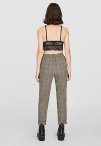 Bralette en dentelle noire associé à un pantalon beige à carreaux taille haute. Le pantalon possède une ceinture élastique et se resserre aux chevilles. Bottes noires épaisses.