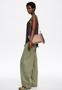 Brązowa skórzana torba na ramię z ozdobami w postaci frędzli, noszona z czarną koronkową bluzką i zielonymi szerokimi spodniami, prezentująca swobodny styl.