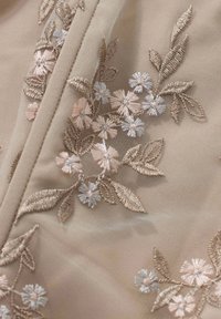 Tissu beige avec une broderie complexe de petites fleurs roses et blanches ainsi que des feuilles brun clair, formant des motifs floraux délicats.