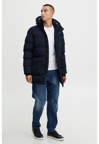 Námořnická prošívaná bunda s kapucí a černými doplňky, vybavená předním zipem, cvočky a velkými kapsami, doplněná bílou košilí.