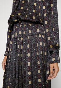 Pitkähihainen, kuviollinen paita, jossa on kireä vyötärö. Ominaisuuksiin kuuluvat geometriset muodot vaaleassa, tummansinisessä ja burgundinpunaisessa pehmeällä kankaalla. Pleatattu yksityiskohta helmassa.