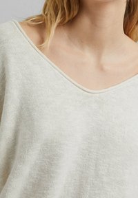 Jasno beżowy sweter dziany o szerokim dekolcie w kształcie litery V, miękkiej fakturze i luźnym kroju, z minimalną ilością szwów oraz casualowym stylem.