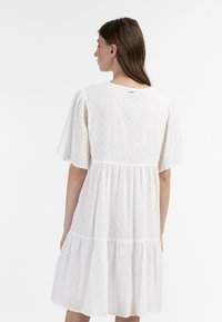 Hvid, knælang kjole med korte pufærmer, tekstureret polka dot stof, samlet lagdelt design og en rund halsudskæring.
