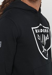 Felpa nera con cappuccio e grande logo bianco "Raiders" che presenta un design con uno scudo argenteo. Include una tasca frontale e un cappuccio regolabile con stringhe.
