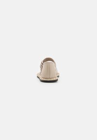 Beige nahk sling-back kingad ümmarguste varvastega, tekstuurse tallaga ja punutud jute aksessuaaridega. Külgedel on hõbedane pandla detail.