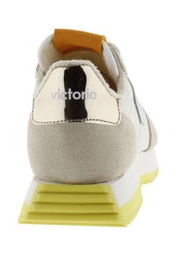 Vue arrière d'une sneaker blanche et beige avec une semelle à nervures jaune et un onglet de talon noir et blanc portant la marque "victoria".