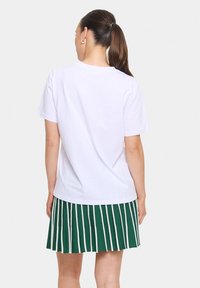 Balta medvilninė T-shirt su apvaliu kaklu, derinama su žalios spalvos klostuota sijonu, turinčiu baltas vertikalias juostas. Paprastas ir neformalios laukimo dizainas.
