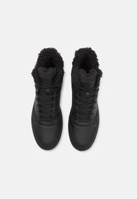 Zapatillas altas negras con un exterior de cuero suave y forro de felpa. Presentan cordones, perforaciones en la puntera y un logo en la lengüeta.