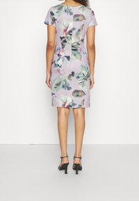 Blommönstrad klänning i lila med en figurnära silhuett, korta ärmar och slät textur. Har en vertikal söm ner längs ryggen.