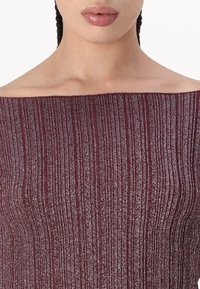 Burgundiški off-the-shoulder marškiniai su grioveliais ir metaliniais siūlais, turintys tiesų iškirpimą ir prigludusį dizainą.