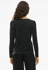 Svart långärmad topp med en mjuk, glänsande textur. Har påsarmer och en rund halsringning. Lämplig för mångsidig styling.