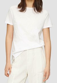 Vit bomulls-T-shirt med en subtil ton-i-ton logodesign på framsidan. Korta ärmar och en avslappnad passform. Kombinerad med ljusfärgade byxor.