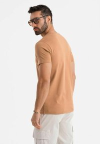 T-shirt marrone aderente con maniche corte, texture di cotone morbido, abbinato a pantaloni cargo di colore chiaro, design minimalista e senza motivi visibili.